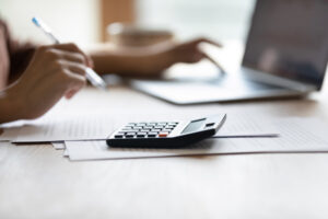 Paying bills. Close up cropped shot of female accountant bookkeeper work at desk on laptop digital calculator. Hands of young woman managing financial papers planning expenses providing payment online